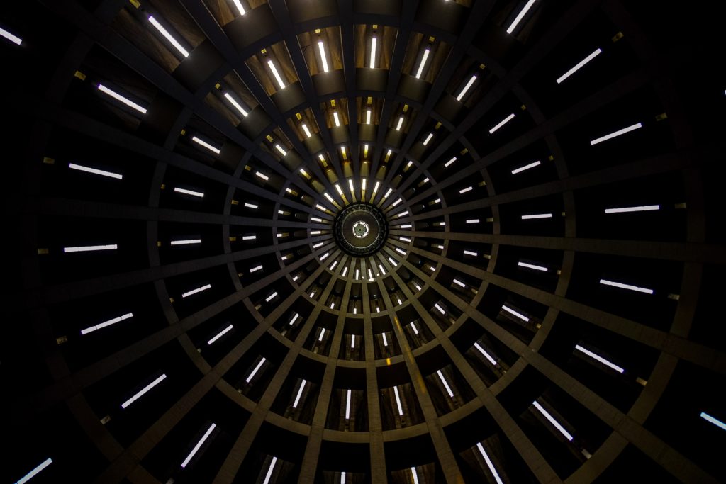 inside of a building looking up at the roof that is a dome shape wit light coming in from different open slots