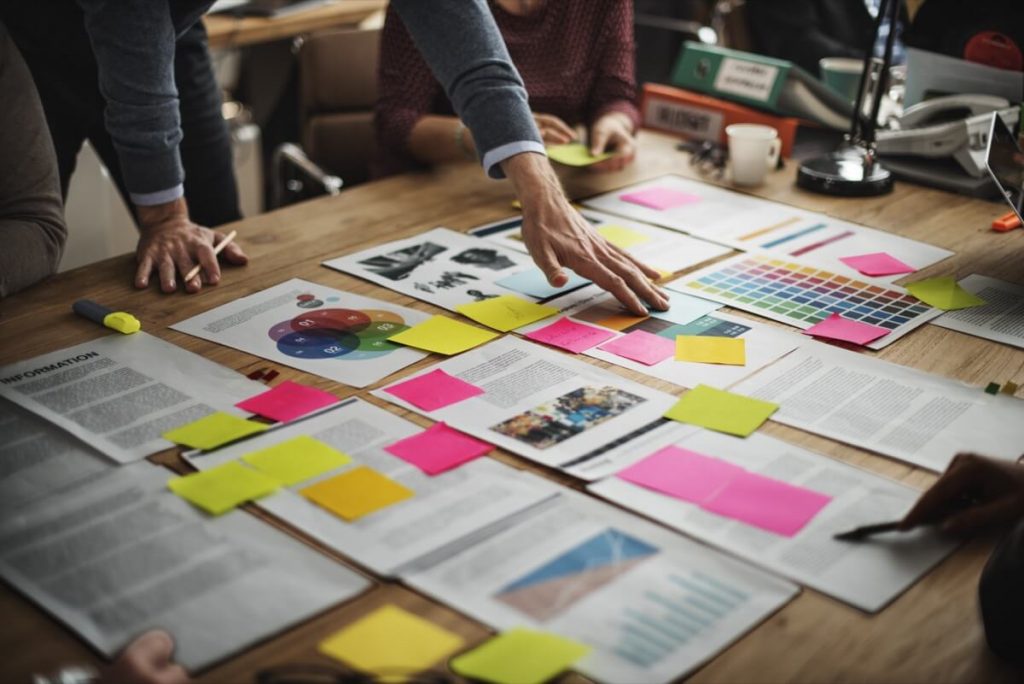 Papers on desk in organized piles with colorful sticky notes on them